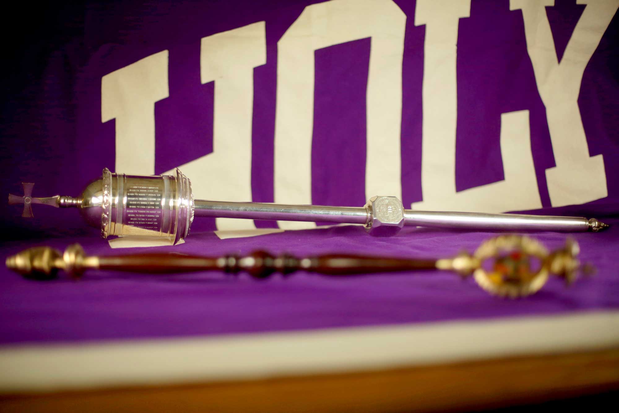 A silver ceremonial mace resting on a purple Holy Cross flag.